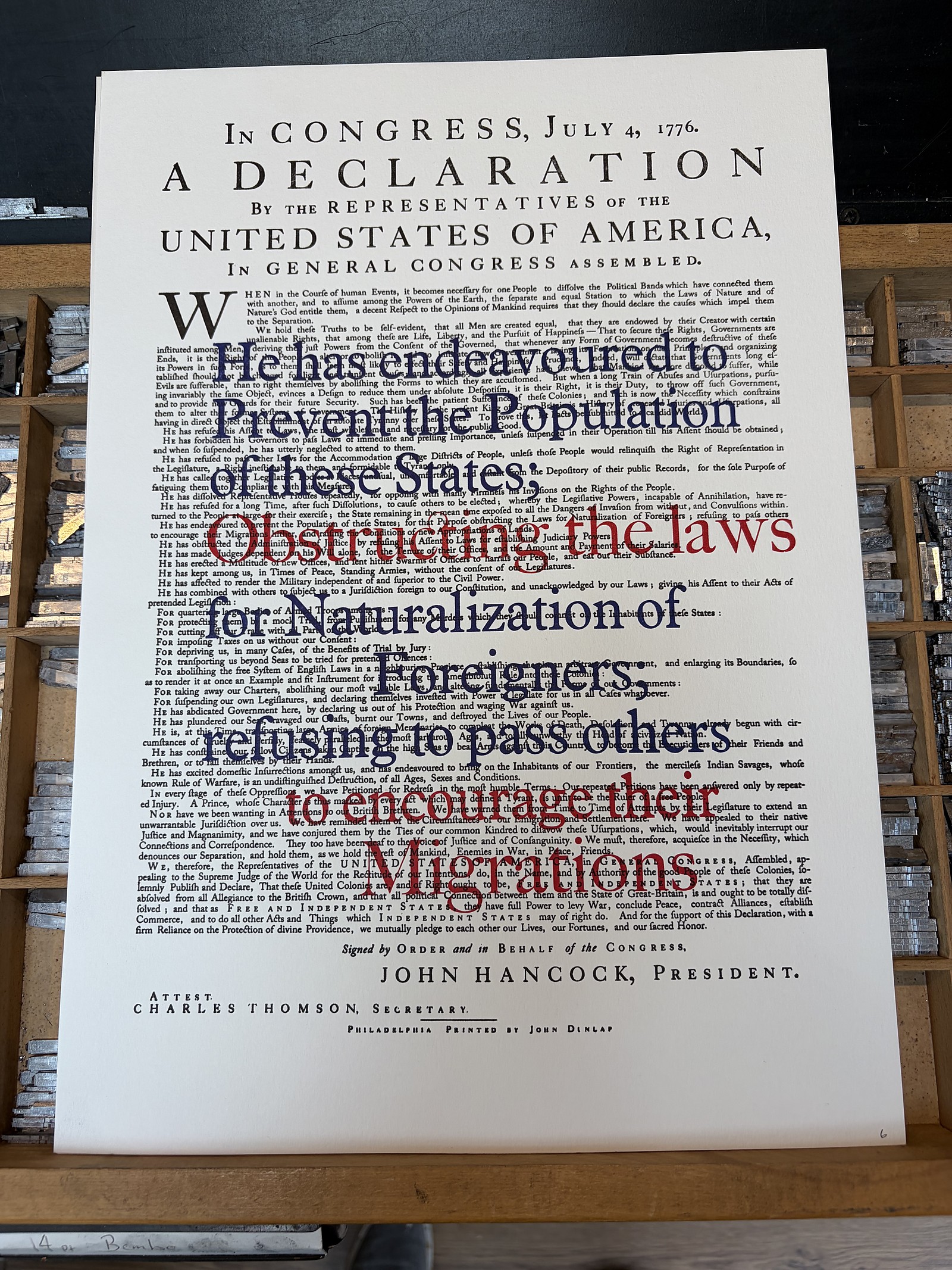 Declaration 250 — the ‘Migration’ overprint in blue and red across the Declaration, resting on a type case: ‘He has endeavoured to prevent the Population of these States…’